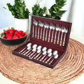 Cutlery set in a maroon box, with strawberries and potted plants in the background.