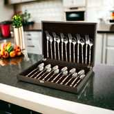 Elegant flatware set in display case, opened on a modern kitchen counter beside colorful vegetables.