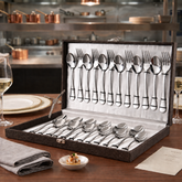 FnS Bria 24-piece stainless steel cutlery set with spoons and forks arranged in a leatherette box on a dining table.