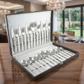 FnS Yearn 26-piece 18/10 stainless steel cutlery set arranged in an open box on an elegantly polished wooden dining table.
