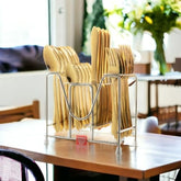 Gold cutlery neatly arranged in a vertical metal rack on a wooden dining table in daylight.