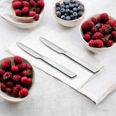 Montavo Trendz 2-pc stainless steel butter knife set displayed on a white napkin, surrounded by bowls of fresh berries.
