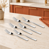 Montavo by FnS Creta stainless steel 6-piece dinner fork set displayed on a cream stone table in a terracotta kitchen.
