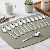 Montavo by FnS Divine 12-piece stainless steel dinner spoon set arranged on a sage green mat over a bright marble counter.