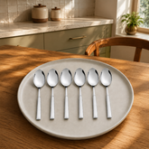 Montavo by FnS Lisbon set of 6 stainless steel baby spoons on a ceramic plate in a warm, sunlit sage-green home kitchen.