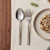 Montavo by FnS Lush 12-piece laser-engraved stainless steel spoon and fork set beside a risotto plate on a dining table.