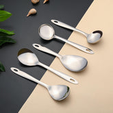 Montavo by FnS 5-piece stainless steel serving tools set arranged on a black and beige surface with decorative leaves.