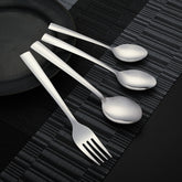 Modern flatware set with sleek, angular handles laid diagonally on a textured black table mat.