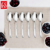 Six FNS Divine stainless steel baby spoons arranged on beige linen with fresh berries in white bowls, premium baby feeding flatware