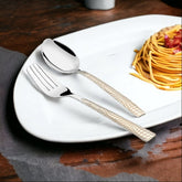 Elegant spoon and fork with patterned handles placed on white plate beside neatly twirled spaghetti.