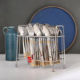 Full cutlery set in silver stand placed on table with decorative jug and blue circular backdrop.