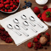 FNS Flair 6-piece stainless steel baby spoons with mirror-polished finish displayed on white linen napkin with fresh strawberries, blueberries, blackberries and mixed berries on rustic wooden table