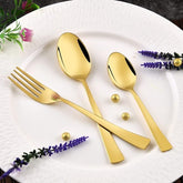 Elegant gold spoon, teaspoon, and fork on a white plate decorated with lavender and golden beads.