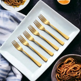 Six gold forks on white rectangular plate with pasta dishes nearby