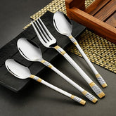Stylish cutlery with golden accents placed on black dish and woven mat in a modern setup.