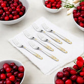 Six stainless steel dinner forks with gold decorative handles surrounded by cranberry bowls