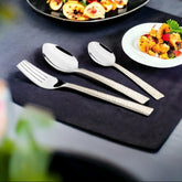 Elegant cutlery set with textured handles on black napkin beside gourmet dishes and white plate.