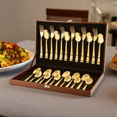 Elegant gold-plated cutlery set in a brown box, displayed on a dining table with food.