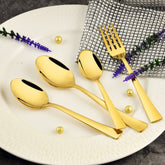 Elegant gold spoons and fork arranged on white plate with silver napkin, flowers, and decorative balls.