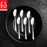 Six Helios baby spoons with textured handles arranged in two rows on black round plate against dark textured background