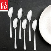 Six Helios dessert spoons with textured handles arranged on dark slate surface next to speckled white plate