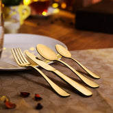 Elegant gold utensils placed beside a white plate on a warmly lit, festive dining table.