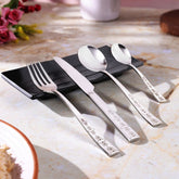 Polished cutlery set with floral handles elegantly placed on black plate on marble tabletop.