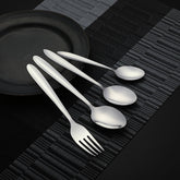 Fork, spoon, and two teaspoons displayed beside matte black plate on dark woven placement.