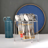 Cutlery set in metal stand placed on a table with blue jug and wall décor behind.