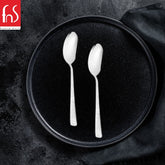 Two Rio baby spoons with smooth mirror finish handles arranged on black round plate with dark textile napkin