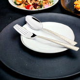 Textured silver fork and spoon with patterned handles placed on stacked white and black plates.