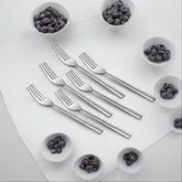 Six stainless steel forks arranged on white cutting board surrounded by small bowls of blueberries