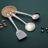 Trinity serving spoons 3-piece set with stainless steel construction displayed on teal background with wooden bowl and decorative shells