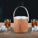 Wooden finish ice bucket with stainless steel rim and handle displayed with two crystal whiskey glasses filled with ice and amber liquid on marble counter