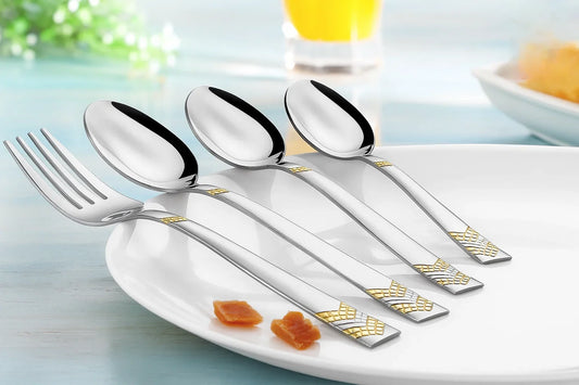 Elegant stainless steel cutlery set with gold-accented handles, including a fork and three spoons, placed neatly on a white plate over a light blue dining table background.