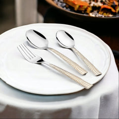 Fork and two spoons with textured silver handles placed on a white ceramic plate at table.