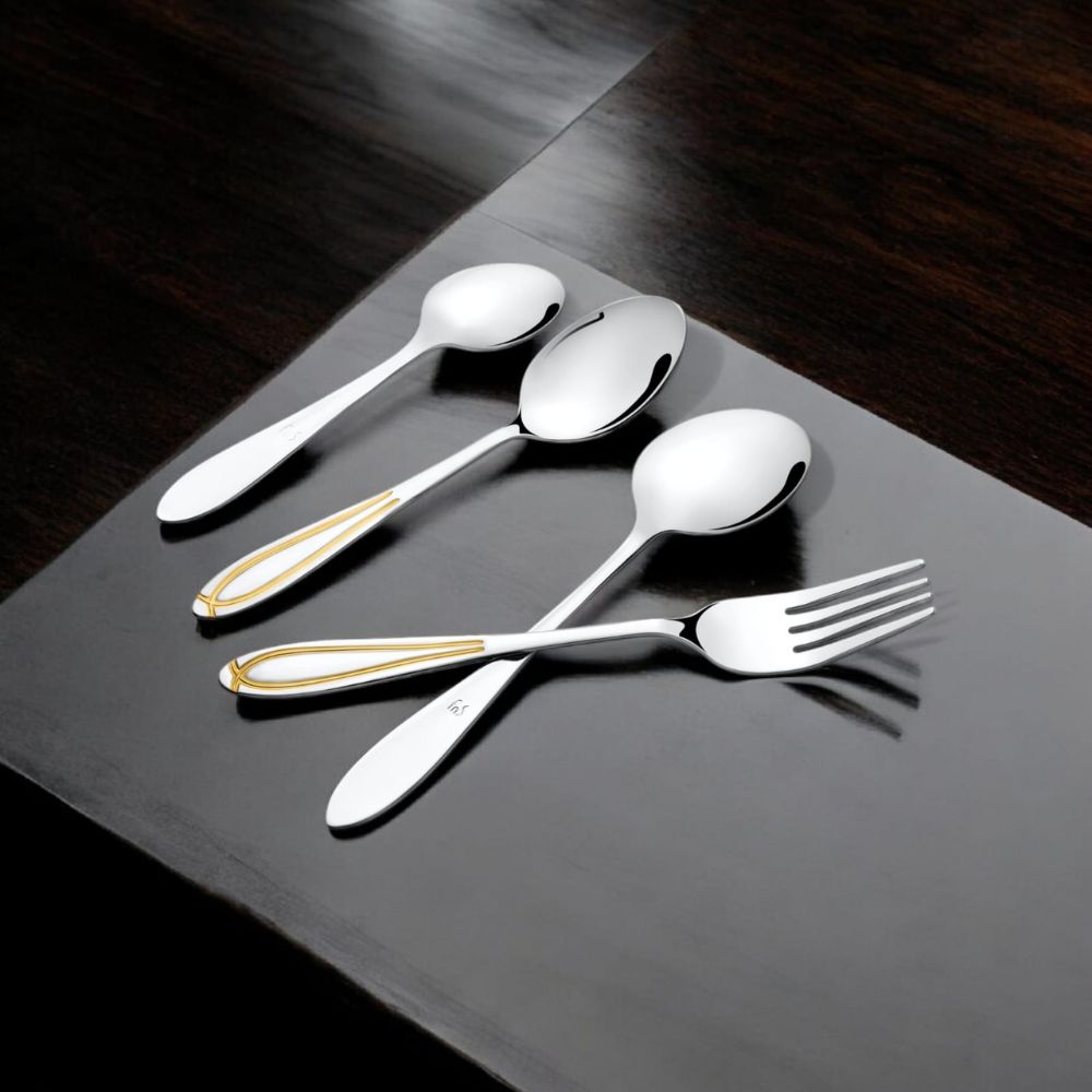 Elegant stainless steel cutlery with golden chevron accents placed on a glossy black wooden surface for a stylish dining vibe.