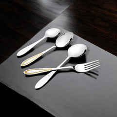 Elegant stainless steel cutlery with golden chevron accents placed on a glossy black wooden surface for a stylish dining vibe.