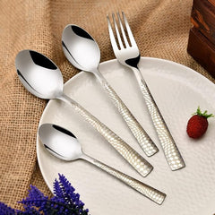 Textured silver cutlery set arranged on white plate with burlap background and decorative strawberry accent.