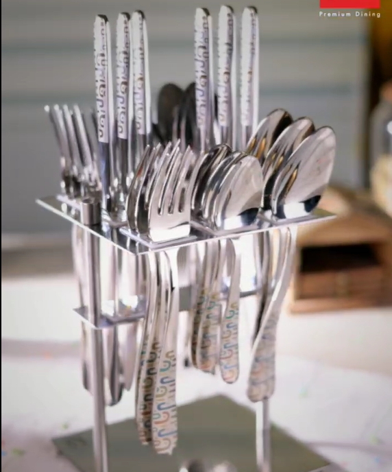 Silver cutlery set with colorful printed handles arranged in a sleek stand on a dining table.
