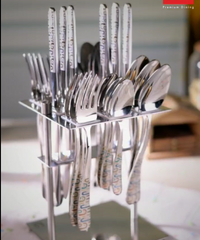 Silver cutlery set with colorful printed handles arranged in a sleek stand on a dining table.