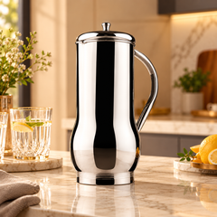 FnS Magnum Everyday Stainless Steel Water Pitcher 1.2 L with mirror finish and lid on a clean kitchen table.
