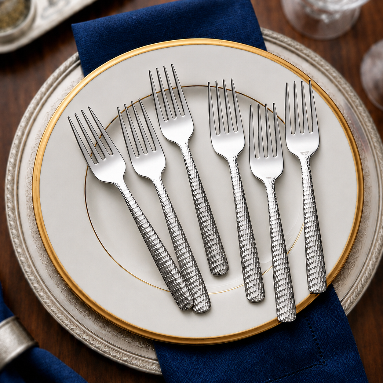 FnS Madrid 6-Pc Stainless Steel Dinner Fork Set with hammered handles arranged on a gold-rimmed plate with navy napkins.