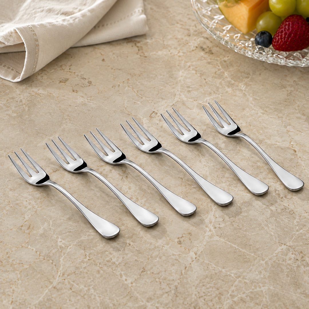 FnS Premium Victoria stainless steel fruit fork set of 6 arranged on a cream marble table with fruit and folded linen.
