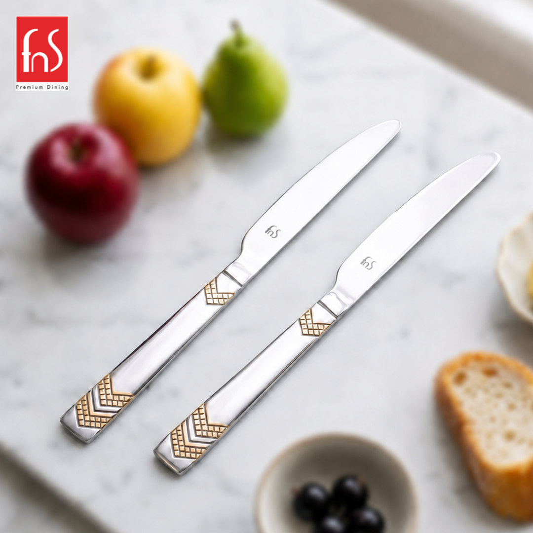 FnS Raga 2-Pc 24K gold-plated stainless steel butter knife set styled with fruit, bread and olives on a marble table.