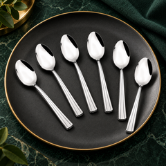 FnS Venice 6-piece stainless steel baby spoon set arranged on a black plate with gold rim against an emerald green backdrop.