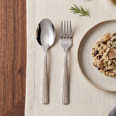 Montavo by FnS Lush 12-piece laser-engraved stainless steel spoon and fork set beside a risotto plate on a dining table.