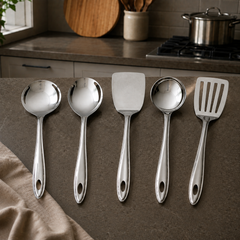 Montavo by FnS Trinity stainless steel serving tools set of 5 displayed on a dark counter in a warm modern home kitchen.
