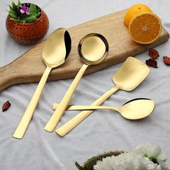 Four Alexa gold serving spoons arranged on wooden cutting board with sliced oranges and decorative flowers