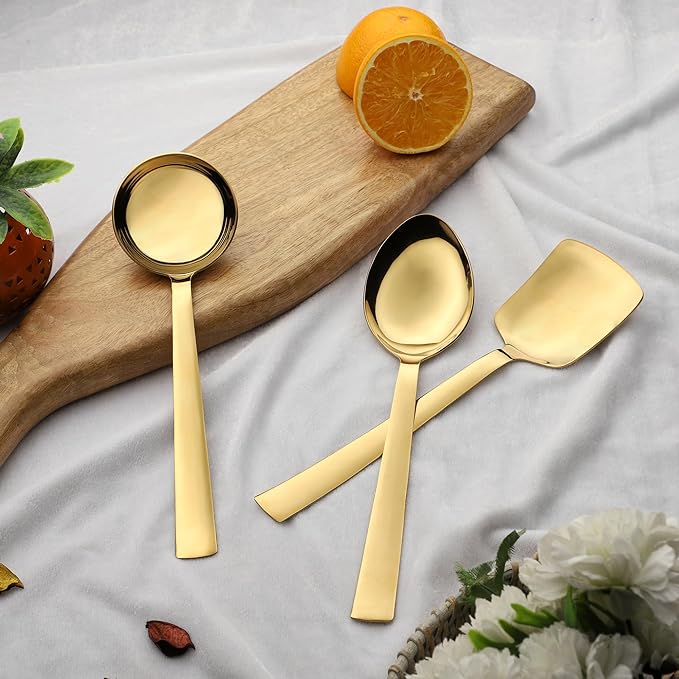 Three gold serving spoons including gravy ladle and rice server displayed on wooden board with fresh orange slices